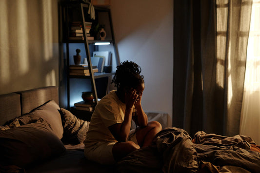 Image: A woman sitting up in bed, crosslegged and with her face resting on clenched fists.