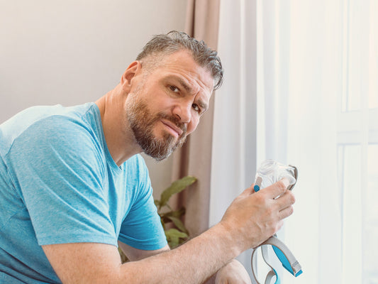 Image: Man holding a CPAP mask and looking uncertain.