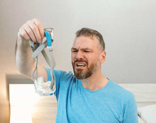 Image: Man holding a CPAP mask in front of his face with a look of disgust.