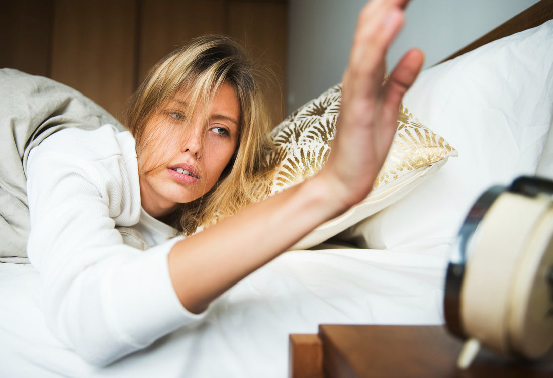 Image: A woman waking up in bed and hitting the alarm clock's snooze button.