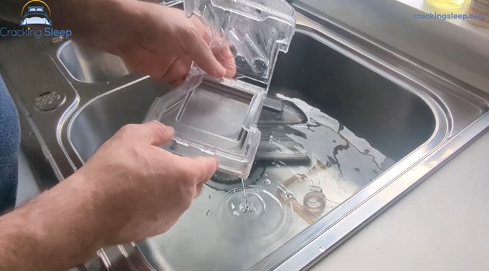 Image: A man cleaning a CPAP humidifier tank in a sink full of water.